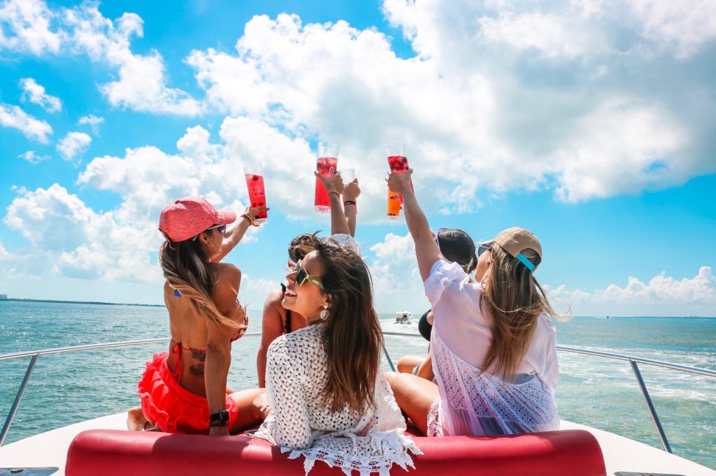 Group of girlfriends on a boat lifting drinks to cheers